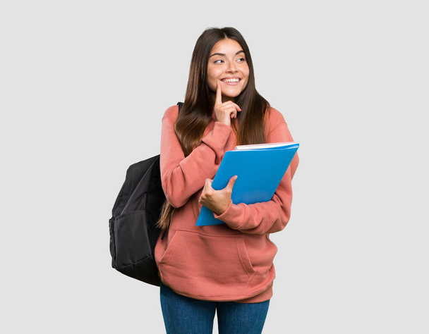 junge Studentin hält Notizbücher in der Hand und denkt über eine Idee nach, während sie über den isolierten grauen Hintergrund blickt - Foto, Bild