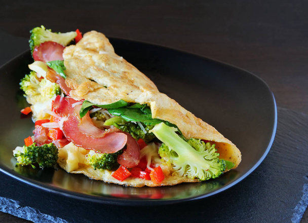 Chutná omeleta se slaninou, sýrem, špenátem a brokolicí na černém talíři - Fotografie, Obrázek