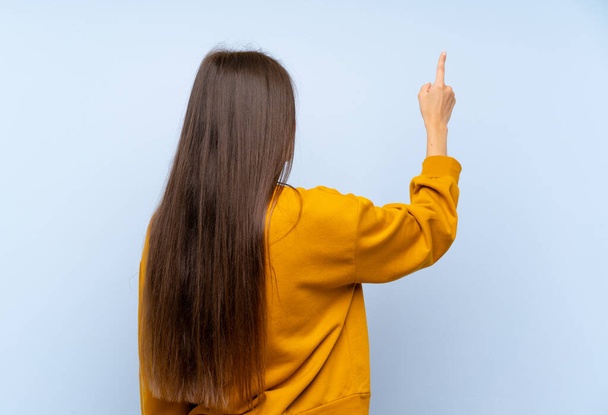 Caucasian young woman over isolated blue wall pointing back with the index finger - Foto, Imagen