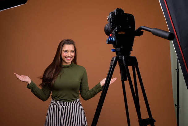 Young beautiful Indian woman vlogging against brown background - Photo, Image