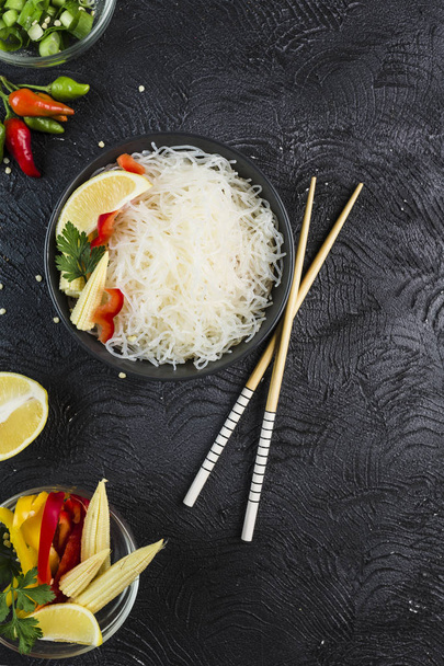 Рисовая лапша фунчоза с овощами в черной миске с отбивными
 - Фото, изображение