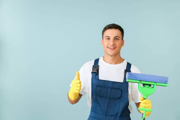 Young man with mop showing thumb-up on color background - Photo, Image