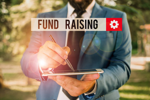 Text sign showing Fund Raising. Conceptual photo the act of seeking to generate financial support for a charity Businessman in blue suite stands with mobile phone in hands. - Photo, Image