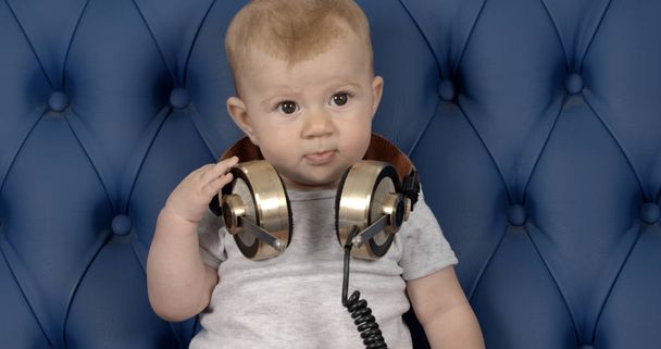 adorable baby girl with large vintage headphones on blue leather sofa - Foto, afbeelding