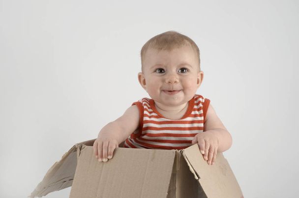 ihana vauva tyttö raidallinen vaatteita istuu pahvilaatikossa
  - Valokuva, kuva