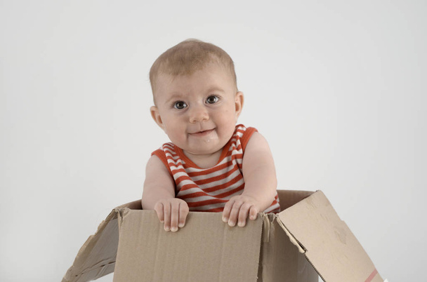 cheerful baby girl in striped clothes sitting in cardboard box  - 写真・画像