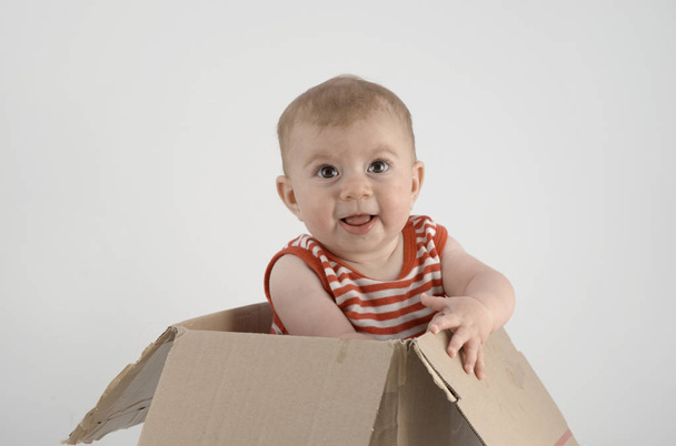 adorable niña en ropa a rayas sentado en caja de cartón
  - Foto, Imagen