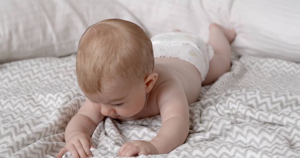 adorável pequena menina com rosto expressivo aprendendo a rastejar na cama
 - Foto, Imagem