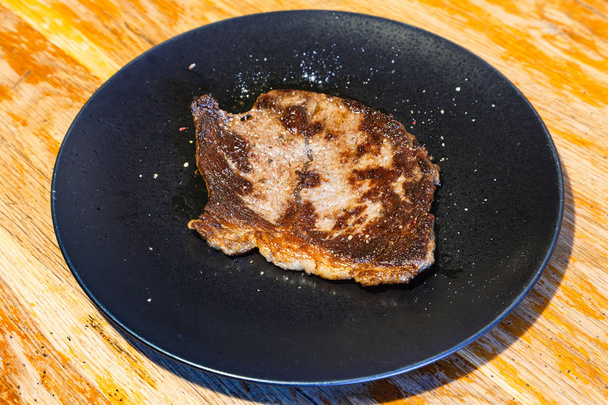 шматок смаженого м'яса на чорній тарілці на столі
 - Фото, зображення