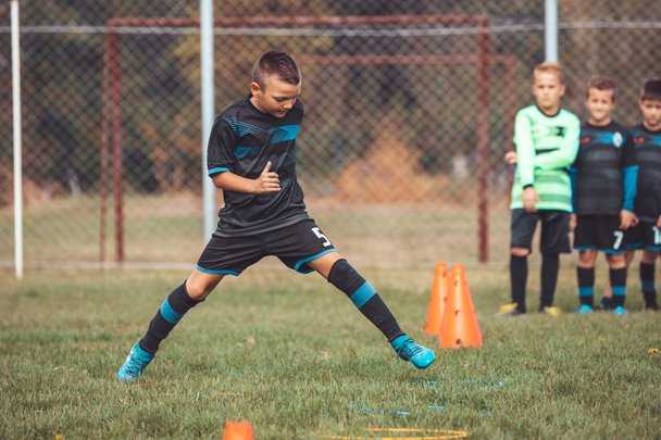 Хлопчик у футбольній майці біжить і стрибає між конусами і кільцем
  - Фото, зображення
