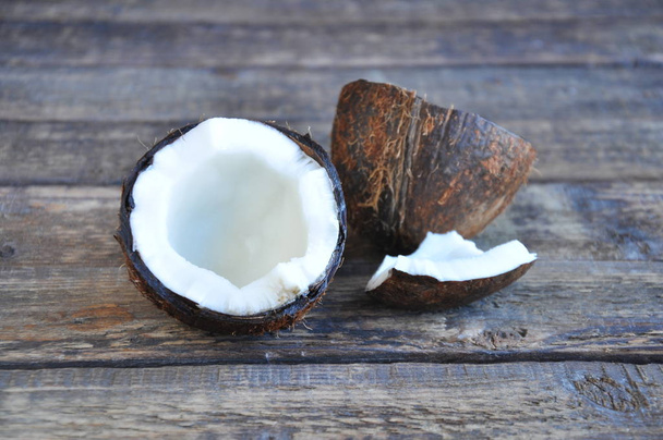 Půl kokosu leží na dřevěném stole. Bílá dužina a kokosová skořápka - Fotografie, Obrázek