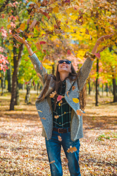 νεαρή όμορφη γυναίκα παίζει με κίτρινα φύλλα φθινόπωρο στο πάρκο της πόλης - Φωτογραφία, εικόνα