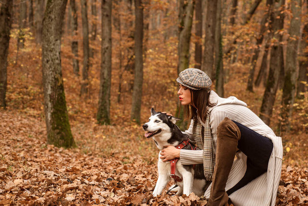 Fashionable glamour woman wearing a hat and long grey sweater playing with her dog. Girl with her pet relaxing outside. Autumn weekend. Autumn model. - Foto, Imagem