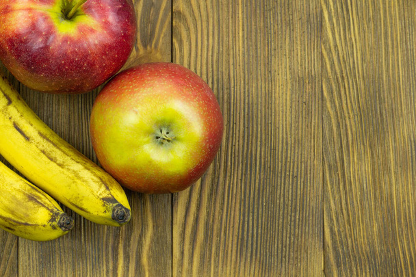 Свежие фрукты. Крупный план красных яблок и бананов на деревянном фоне с копировальным местом для текста
 - Фото, изображение