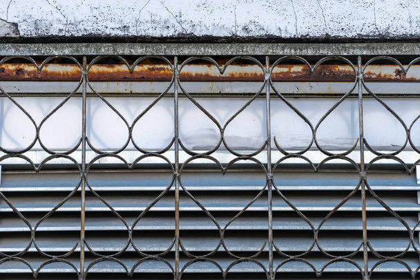 Griglia di sicurezza decorativa in metallo su finestra con ripetitivo a forma di cuore e un dettaglio di vecchia parete intonacata sbriciolata
 - Foto, immagini