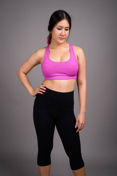 Young beautiful Asian woman ready for gym against gray backgroun - Fotó, kép