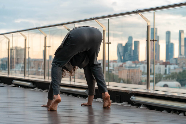 Attractive athletic man practicing yoga in business center with beautiful view on a city from skyscraper. - Fotoğraf, Görsel