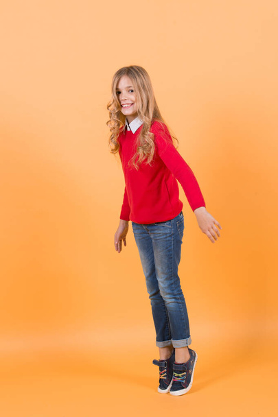 Girl in red sweater and jeans stand on tiptoe - Φωτογραφία, εικόνα