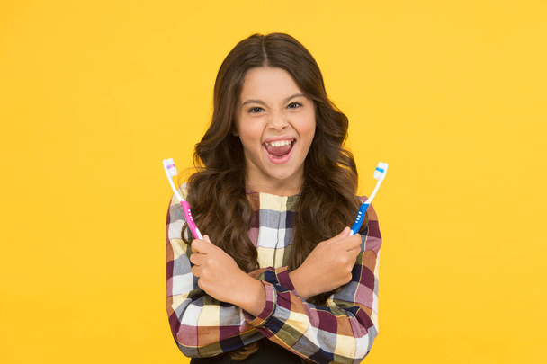 Teeth whitening. Girl cute long hair holds toothbrushes yellow background. Child girl holds two toothbrushes. Child school girl smart kid happy face cares hygiene. Brush teeth concept. Teeth hygiene - Valokuva, kuva