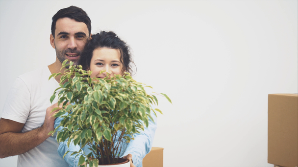 A fiatal pár együtt költözött egy új lakásba. Egy zöld virágcserepet tartanak és mosolyognak. Felvétel, animáció. 4k. - Felvétel, videó