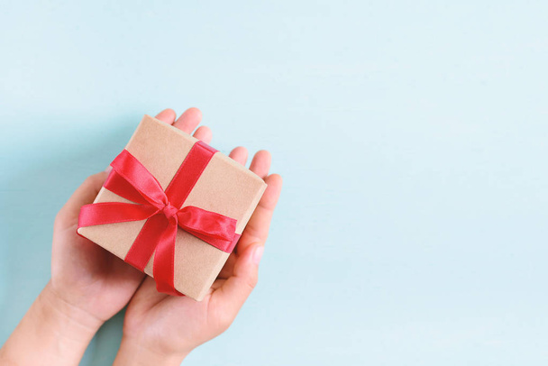Χέρια κρατώντας κουτί δώρου με κόκκινη κορδέλα σε παστέλ φόντο, δώρο για να δώσει σε ειδική ημέρα - Φωτογραφία, εικόνα
