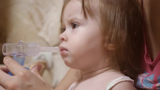 Egy kislány, akit inhalációs maszkkal kezeltek az arcán egy kórházban. a gyermek beteg és inhalátoron keresztül lélegzik. A kisgyermek az influenzát inhalációs gőz belélegzésével kezeli. - Felvétel, videó