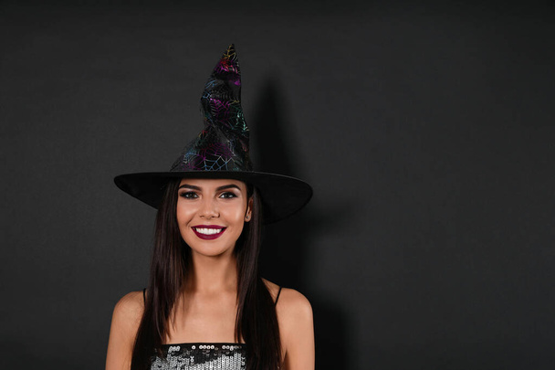 Beautiful woman wearing witch costume for Halloween party on black background, space for text - Photo, Image