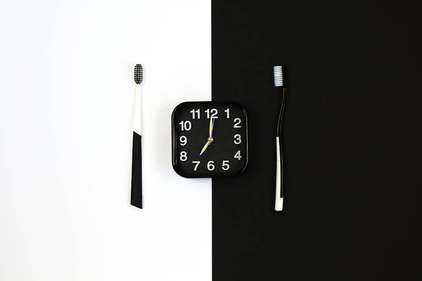 Black alarm clock with manual toothbrush set on white and black background. - Foto, imagen
