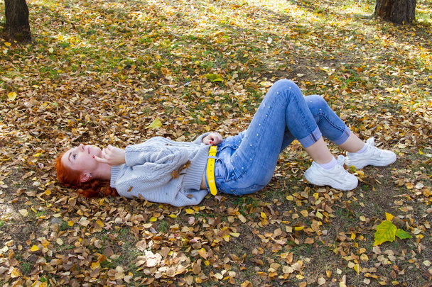 Jeune fille aux cheveux roux se couche sur un feuillage jaune d'automne
 - Photo, image