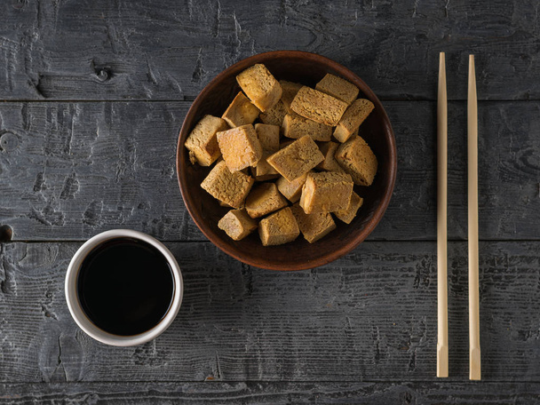 Smażony ser tofu, sos sojowy w białej misce i pałeczki na drewnianym stole. Układy płaskie. - Zdjęcie, obraz