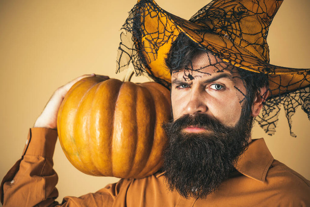 Halloween man with pumpkin - Holidays celebration concept. Scary hipster man with beard in Halloween hat. Bearded Halloween man in witch hat - studio shot close up. - Foto, imagen