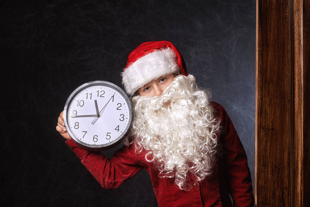 Retrato de un niño en un sombrero de Santa Claus con un reloj que indica la hora
 - Foto, imagen