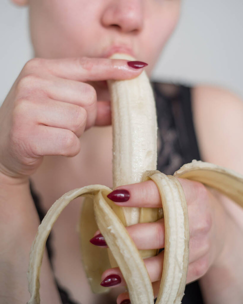 Close-up of the face, lips, tongue of a young, European girl licking a big yellow, sweet banana. - Φωτογραφία, εικόνα
