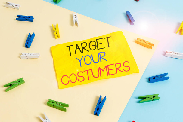 Pismo pisma Target Your Costumers. Koncepcja oznacza konkretny zakres i zainteresowania potencjalnych użytkowników i kupujących Kolorowy papier szpilka pusty przypomnienie żółty niebieski podłogi tło biuro. - Zdjęcie, obraz