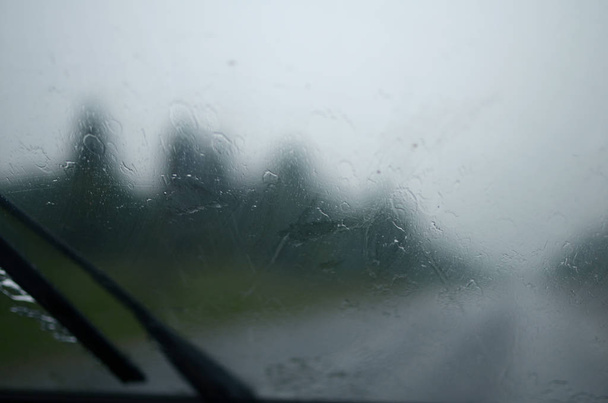 auton märkä tuulilasi, joka raskaassa kaatosade ratsastaa tiellä huonolla näkyvyydellä. varovaisuus, hätätilanne
 - Valokuva, kuva