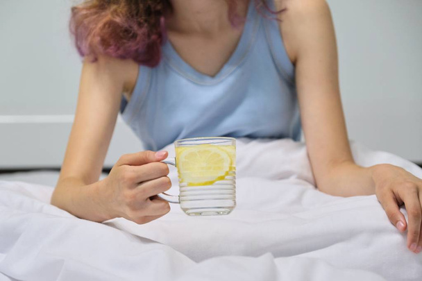 Teen girl sitting in bed in morning with glass of water with lemon - Foto, imagen