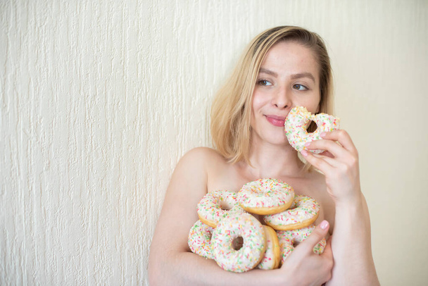 Nude young woman eating donuts. Portrait of an attractive woman with a mountain of donuts - Foto, Bild