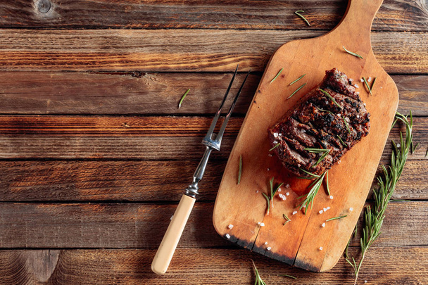 Grilled ribeye beef steak with rosemary and salt on a wooden bac - Фото, зображення