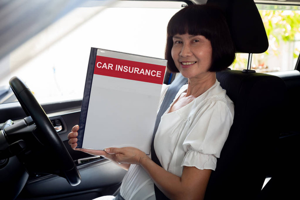 Mujer mayor asiática feliz sosteniendo libro de documentos de seguro de coche y sentado en el coche, vehículo de seguridad y protección concepto de persona cliente
 - Foto, Imagen