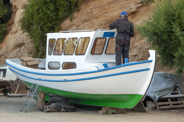 Old fishing boat getting repaired in an greek harbour by one worker - Photo, Image