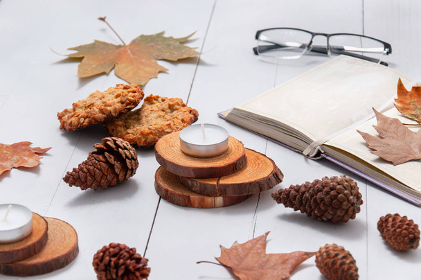 本は、白、古い、木製のテーブルの上に木製のサポート、コーンと乾燥した葉の上に開いている、眼鏡、小さなろうそくです。秋の快適さ. - 写真・画像