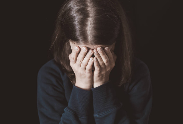 Femme pleure couvrant son visage avec ses mains sur un fond noir. Violence familiale
. - Photo, image