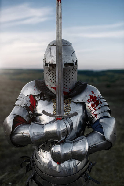 Medieval knight in armor and helmet poses with sword, great battle. Armored ancient warrior in armour posing in the field - Photo, Image