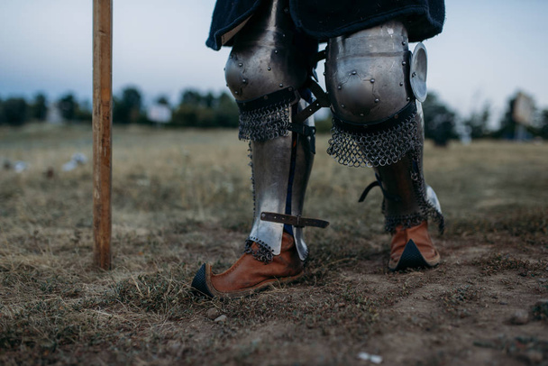 Μεσαιωνικά πόδια ιππότη σε μεταλλική πανοπλία, πίσω όψη, μεγάλο τουρνουά. Τεθωρακισμένος αρχαίος πολεμιστής με πανοπλία ποζάρει στο πεδίο - Φωτογραφία, εικόνα