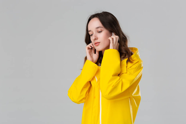 Brunette girl wearing yellow raincoat dancing listening to music with wireless earbuds. Concept of enjoying life. - 写真・画像