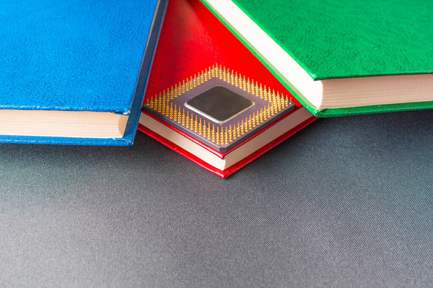The processor from the computer lies between the multicolored books - Foto, Imagem