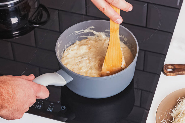 Hand mixing creamy risotto with cheese in a pot close-up. - Foto, Bild