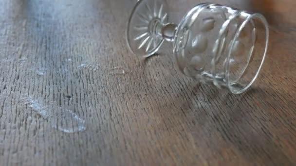 An empty crystal wineglass sways on the wooden surface - Filmati, video