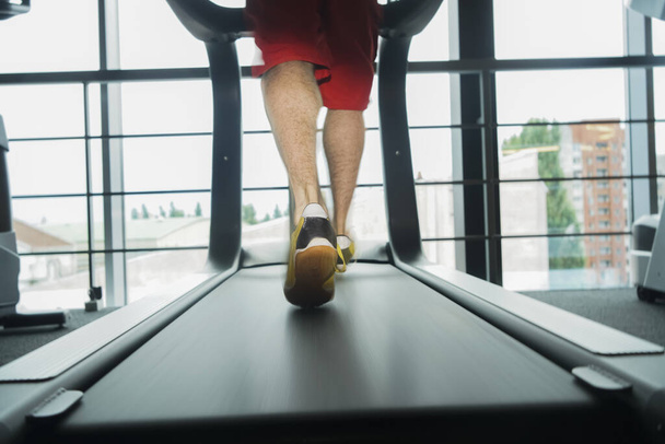 Theme of sport and weight loss. Close-up of t young strong man in a white and black sneakers on a simulator, running in the gym - Fotografie, Obrázek