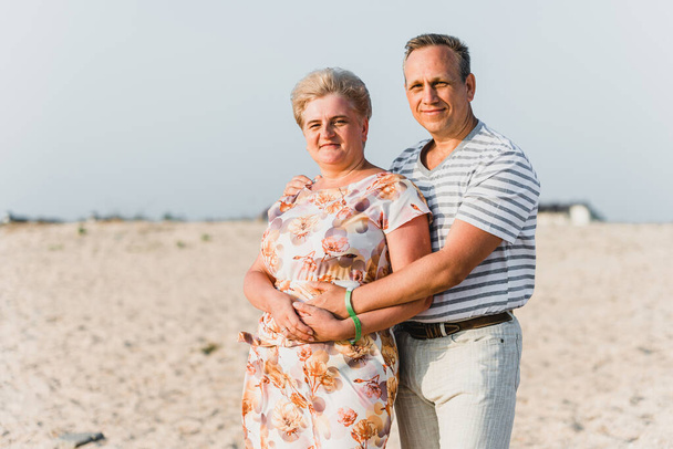 Romantic adult couple standing together on the beach. Mature pair relax at the seaside on holiday. Happy familiy walking and holding hands near sea. Husband embracing wife. Love story near the sea - Fotoğraf, Görsel